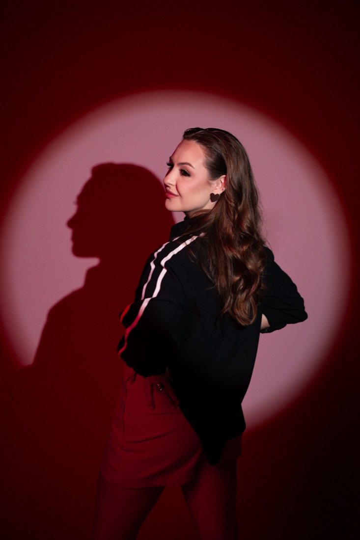 Dra. Ana Purr de perfil sob um foco de luz, com sua sombra projetada ao fundo